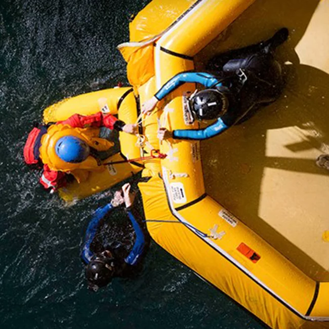 Trainees in an indoor pool swimming towards the inflatable boat in a RelyOn training center