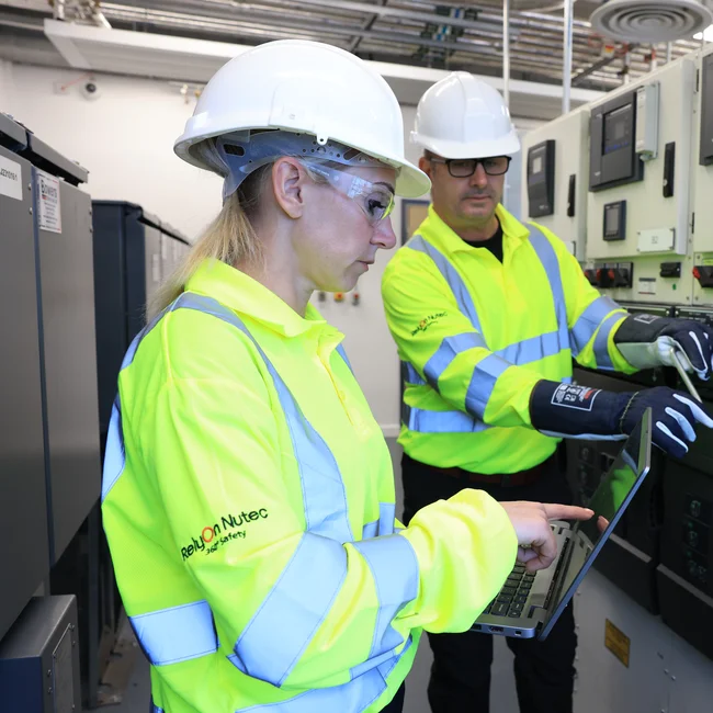 Two trainees in an electrical room, pointing at laptop and equipment
