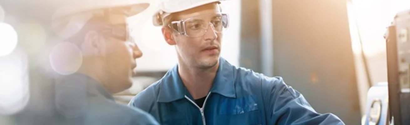 Men in safety gear talking in front of a panel